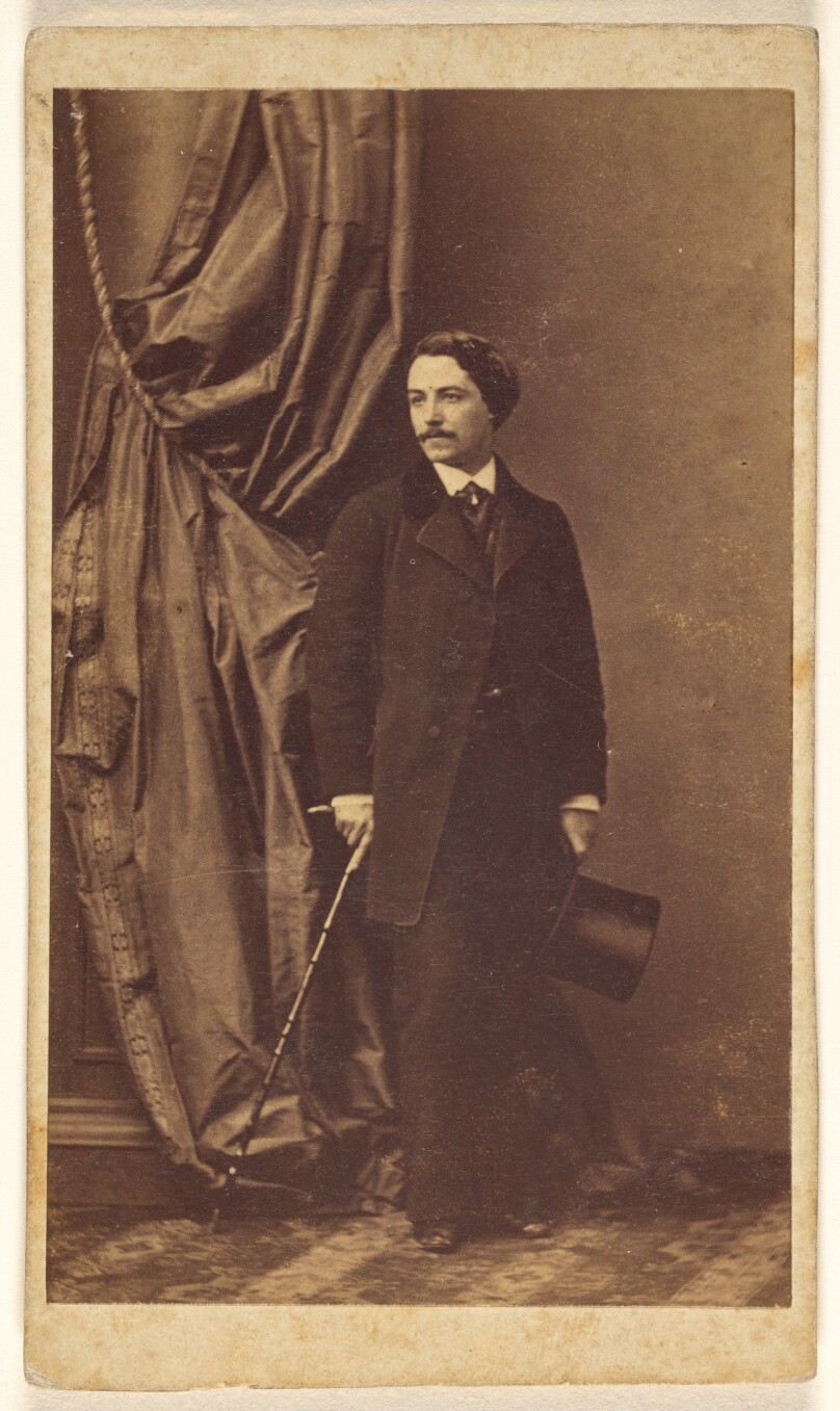 [Unidentified man with moustache standing, holding a top hat in one hand and a cane in the other]