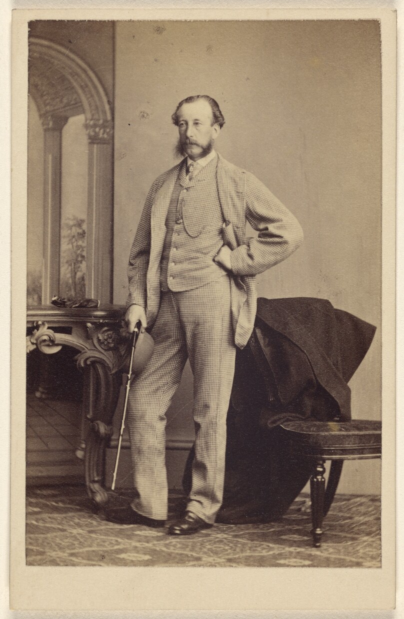 [Unidentified bearded man standing, holding a walking stick]