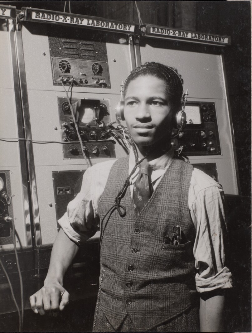 [Man wearing headphones stands in front of a large machine]
