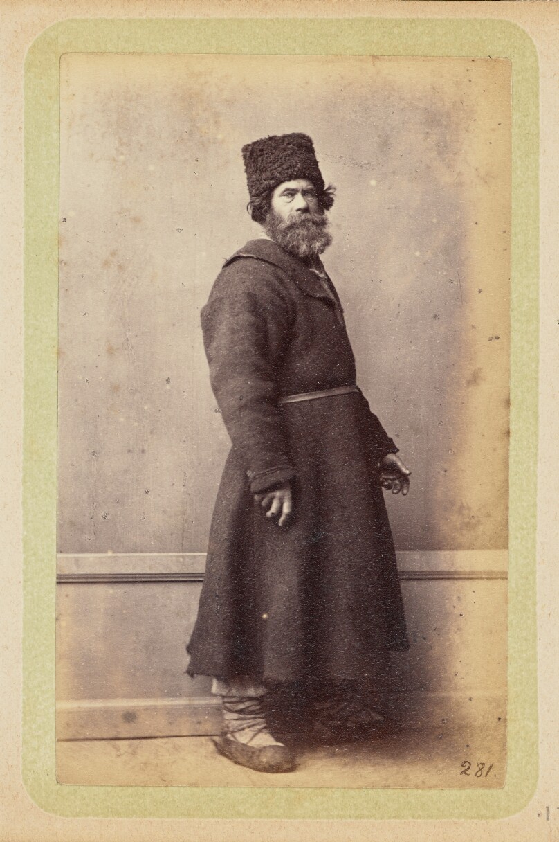 [Bearded man posing in long, dark coat and wool hat]