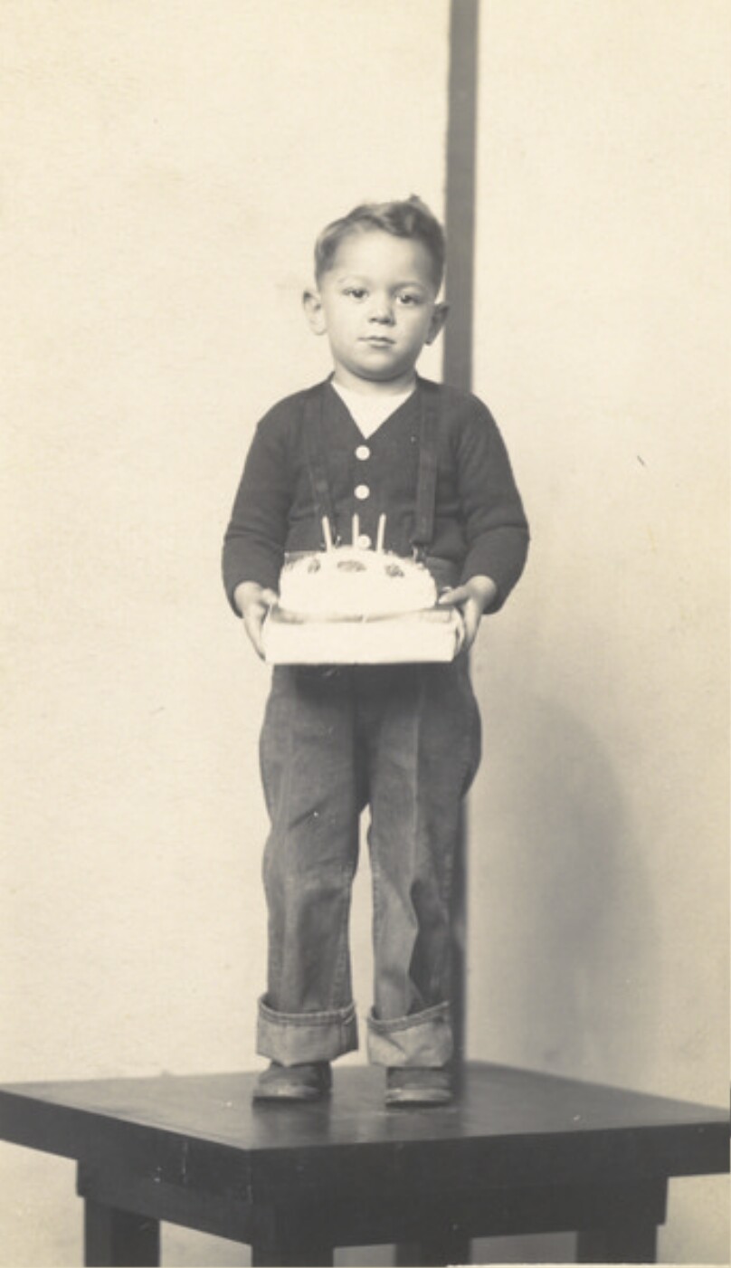 Untitled (boy, standing on table, holding birthday cake)