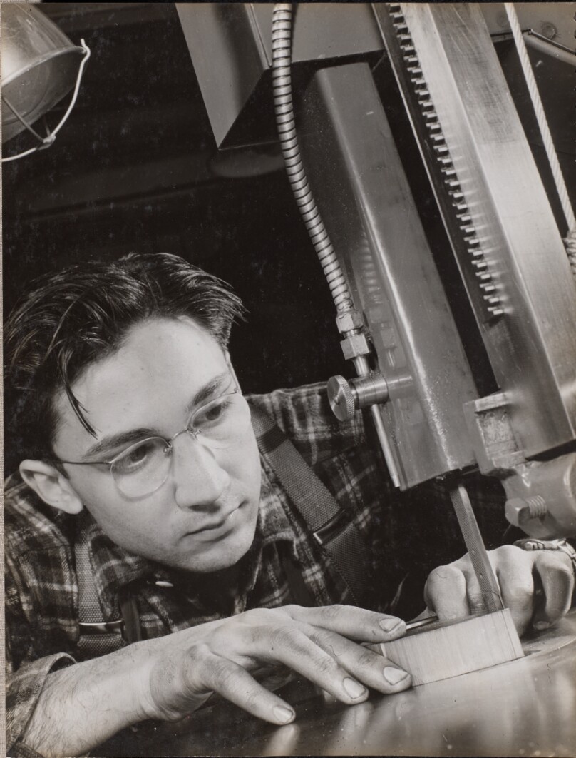 [Man wearing glasses works intently with an industrial file]