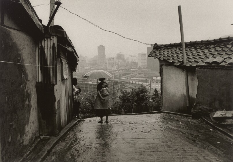 [Girl with Baby on Her Back While Holding an Umbrella and Looking Out Over the City of Seoul]