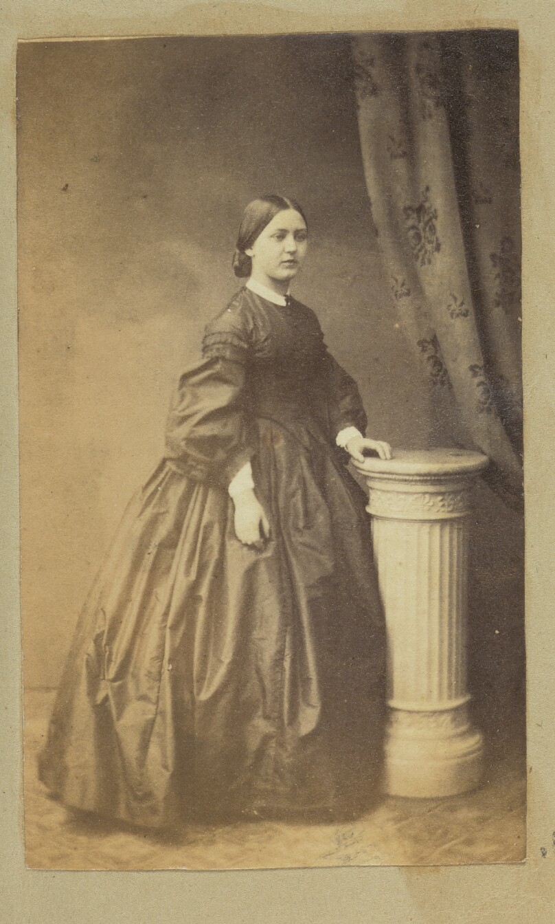 [Portrait of woman standing next to pedestal]