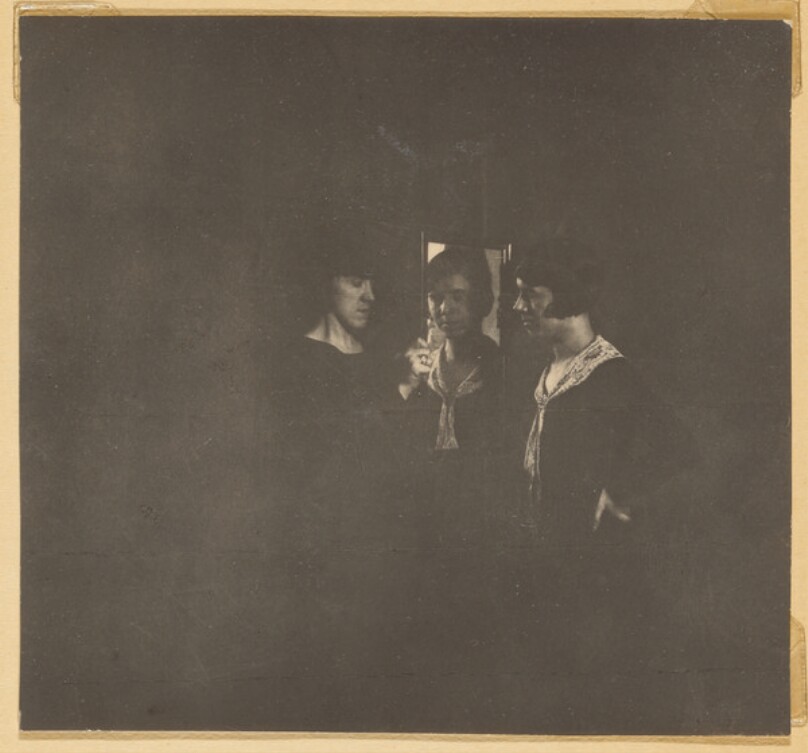 [Three women gathered around flower]