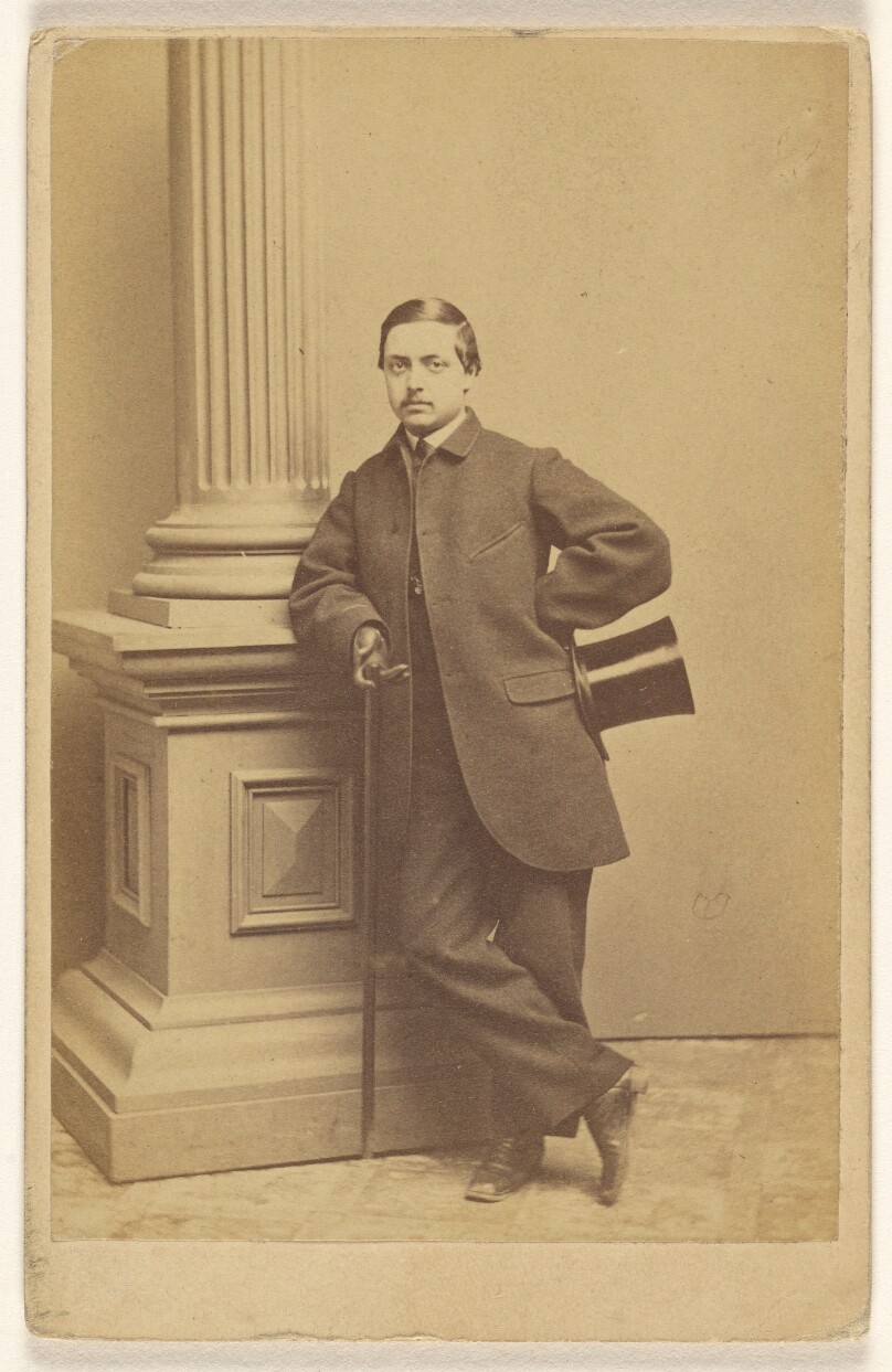 [Unidentified man with moustache standing, holding a top hat in one hand, a cane in the other]