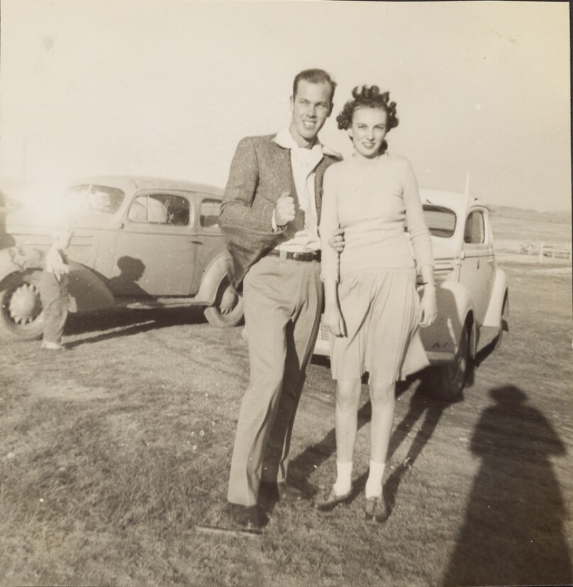 [Couple posed in front of cars]