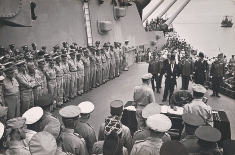 The Japanese surrender on board the USS Missouri in Tokyo Bay - General Yoshijiro Umezu signs the surrender document while General MacArthur looks on.