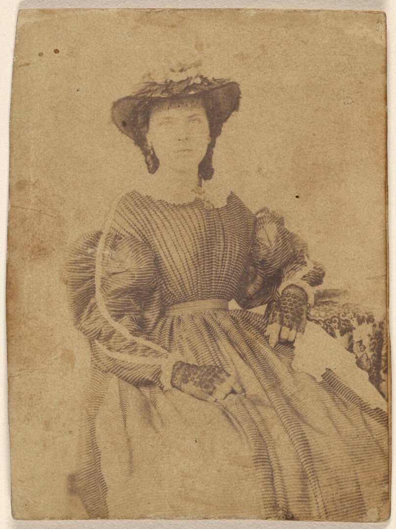 [Unidentified woman wearing a hat and open-fingered gloves, seated]