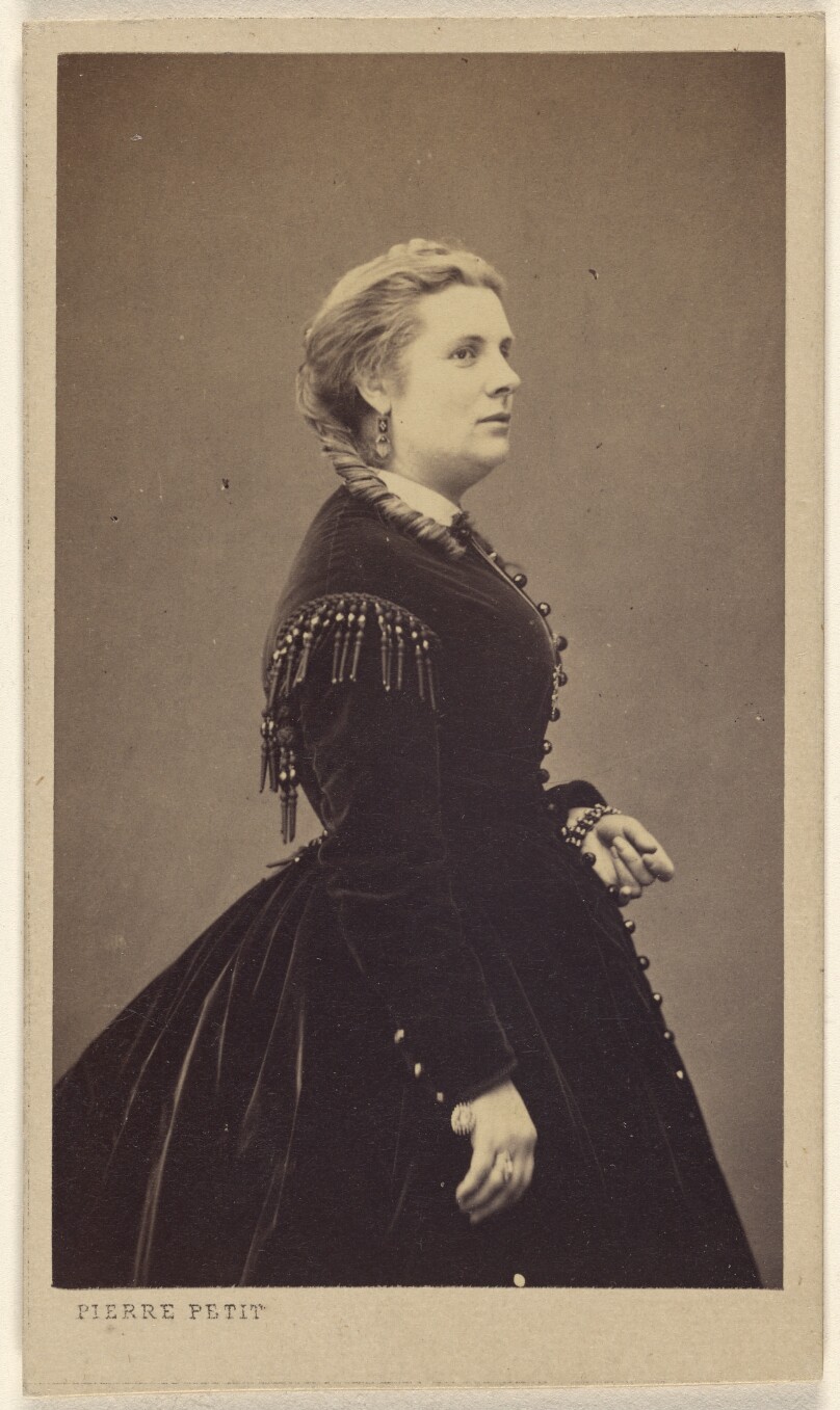[Unidentified woman wearing a dark dress, standing, in profile]