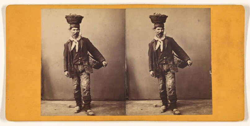 [Man standing, smoking pipe, with basket on head and another under one arm]