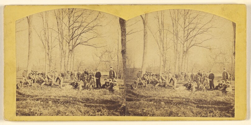 [Large group of men at open field with barren trees]