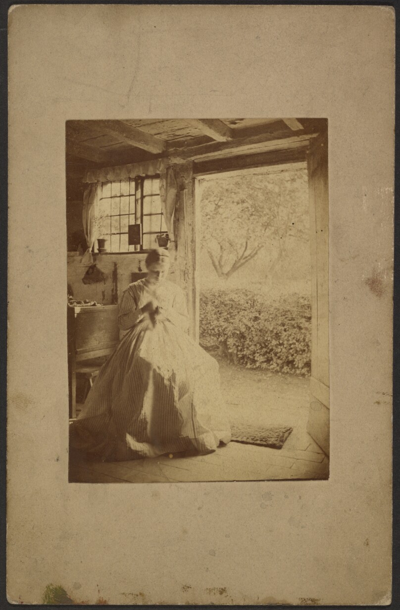 [Woman in long striped dress seated inside room]