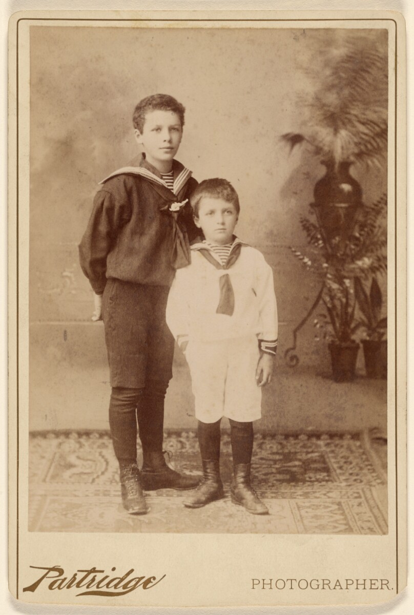 [Two young boys standing, both wearing sailor-type outfits]
