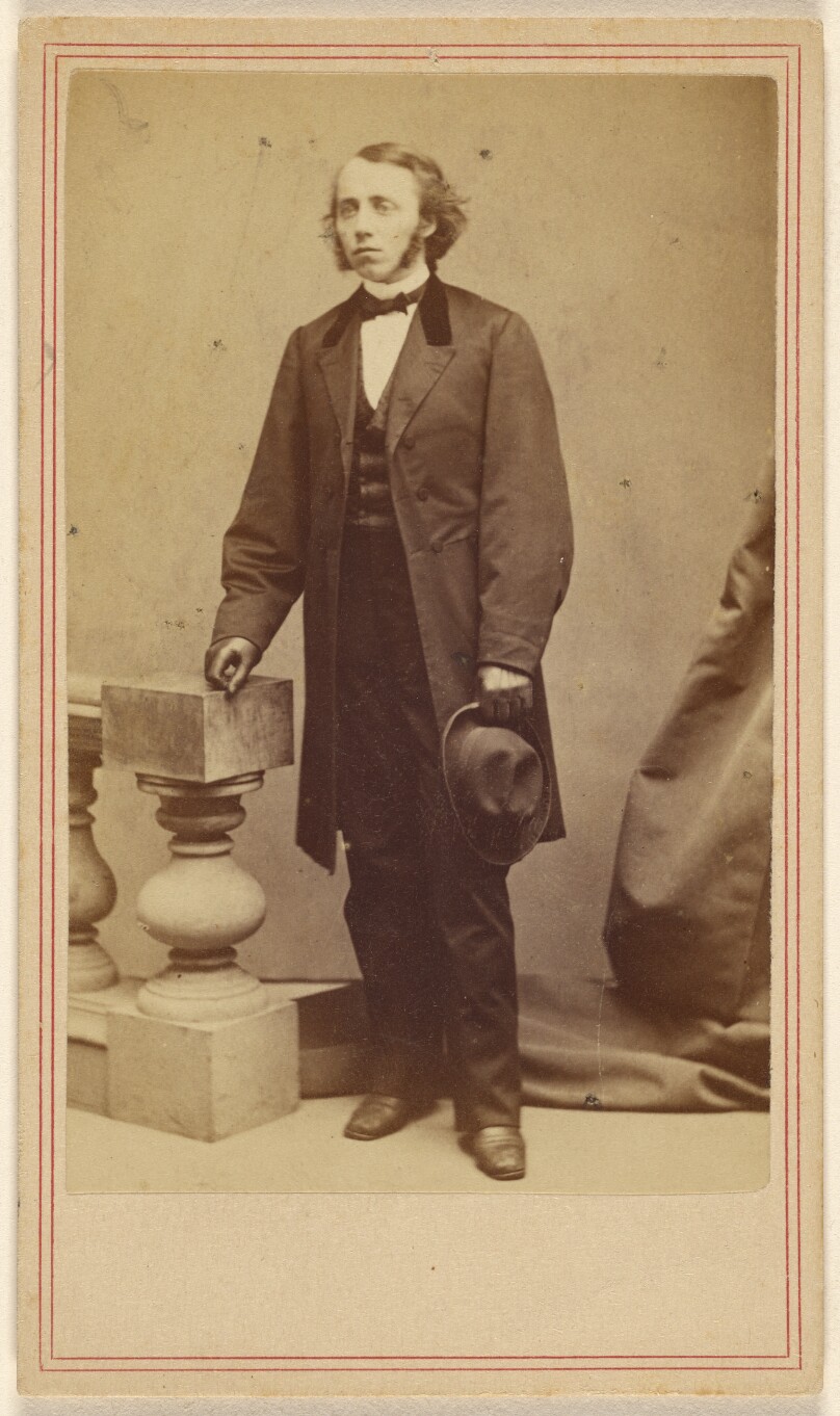 [Unidentified man with long sideburns, standing, holding his hat in his left hand]