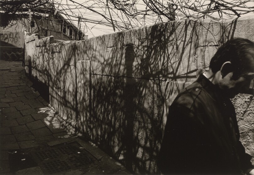 [Man in Dark Jacket Walking Past Stone Wall]