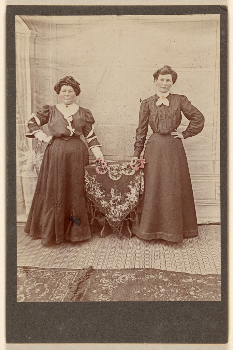[Two women standing at a table holding flowers]