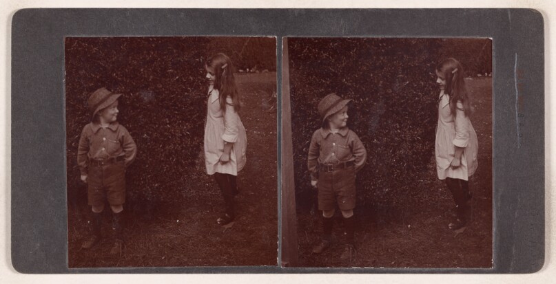 [Unidentfied little boy wearing a hat and a little girl standing in the yard] (recto); [Little boy blowing up a balloon] (verso)
