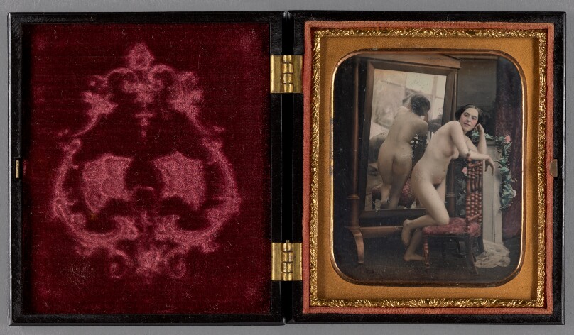 [Female nude standing with back to full-length mirror]