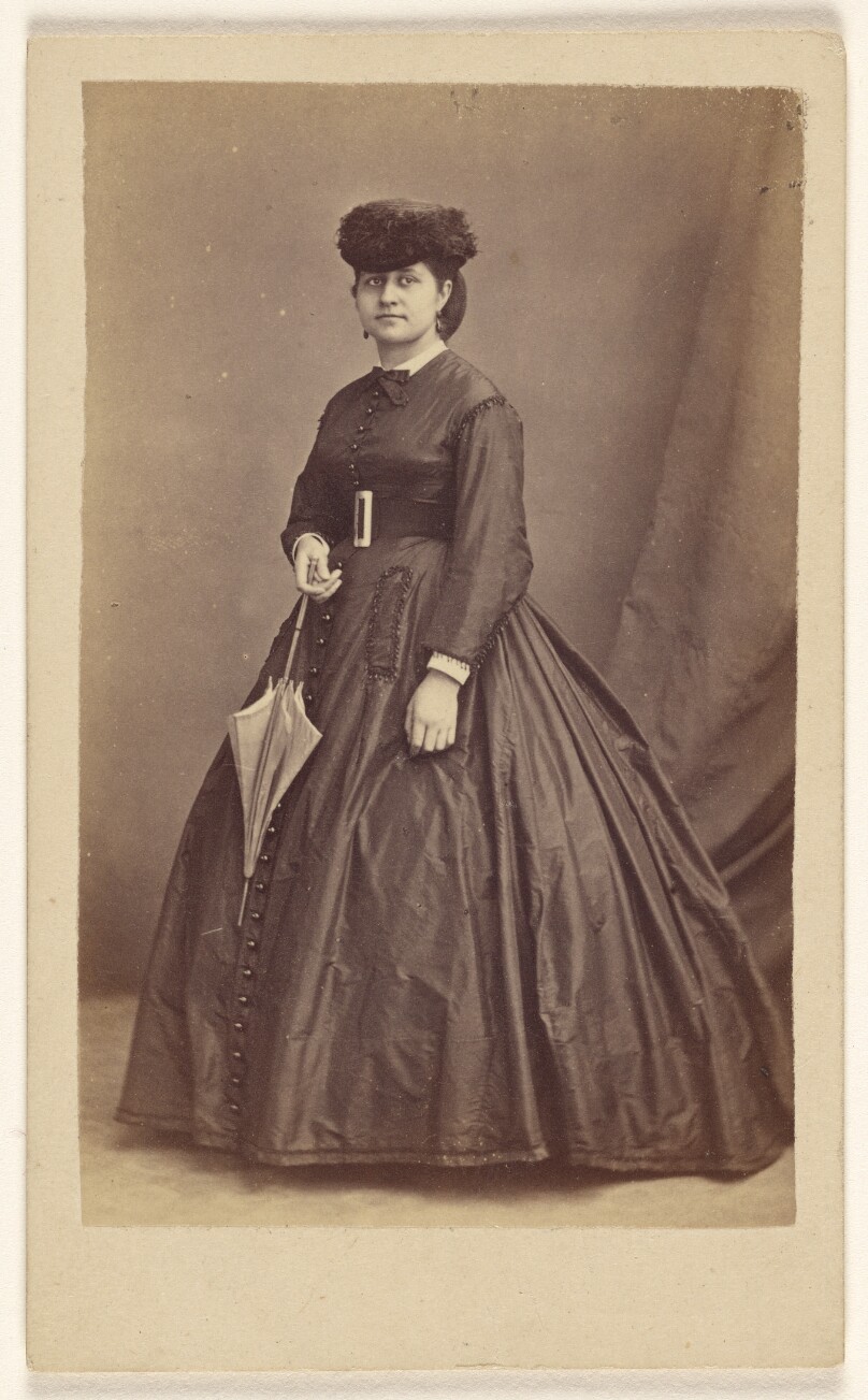 [Unidentified woman wearing a dark hat, holding a parasol, standing]