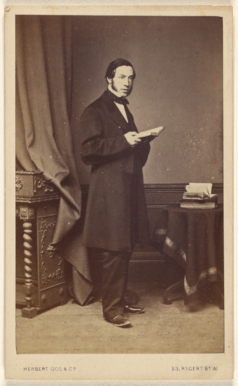 [Unidentified man with long sideburns standing with an open book]