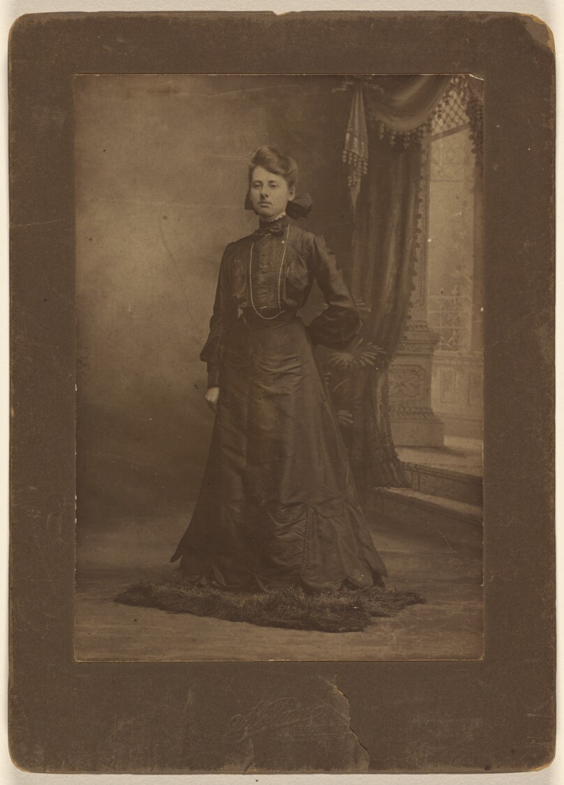[Portrait of a young woman in long black dress, standing]
