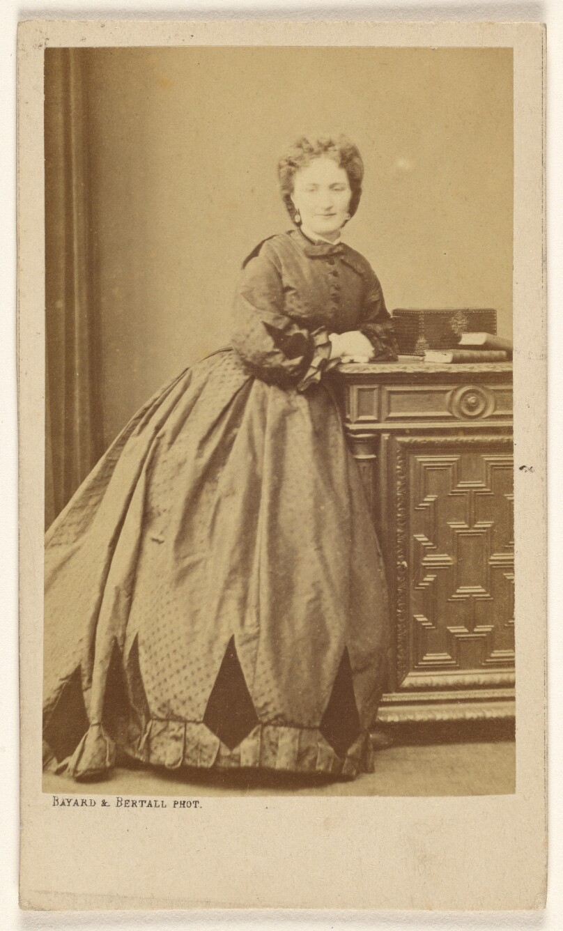 [Unidentified woman standing, leaning against a credenza]