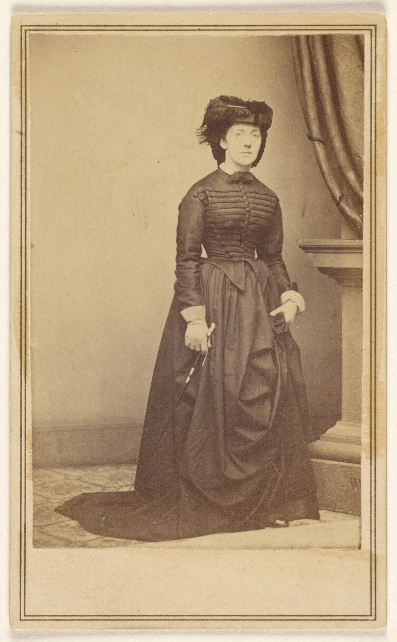 [Unidentified woman wearing a hat and long dark dress.]