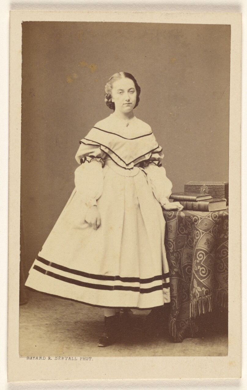 [Unidentified woman standing near a table with books on top]