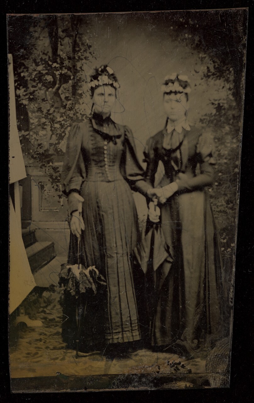 [Two unidentified women, standing, both wearing hats and holding parasols]