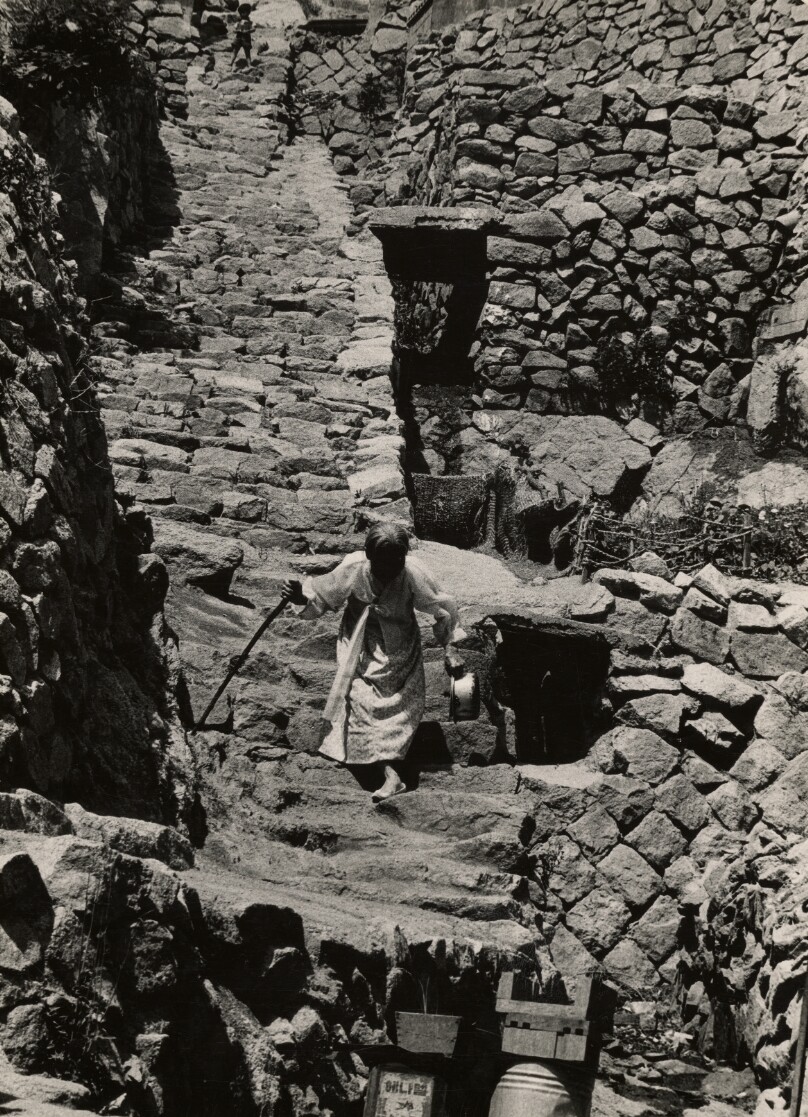 Elderly Woman Climbing Down Stone Stairs with a Walking Stick