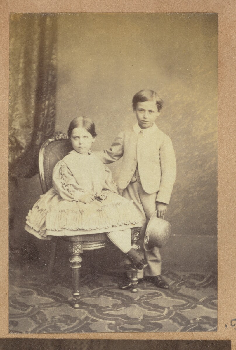 [Portrait of two children posed with chair]