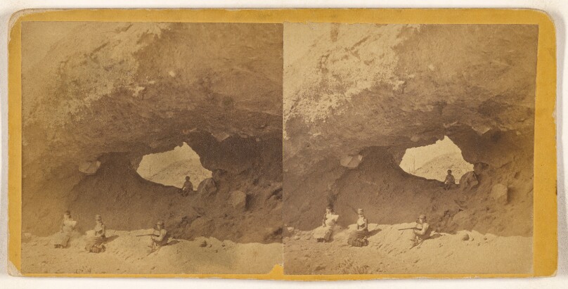 [Group of four sitting near rock structure with hole at center]