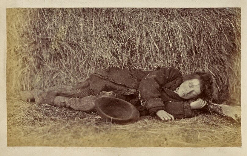 [Boy sleeping next to haystack]