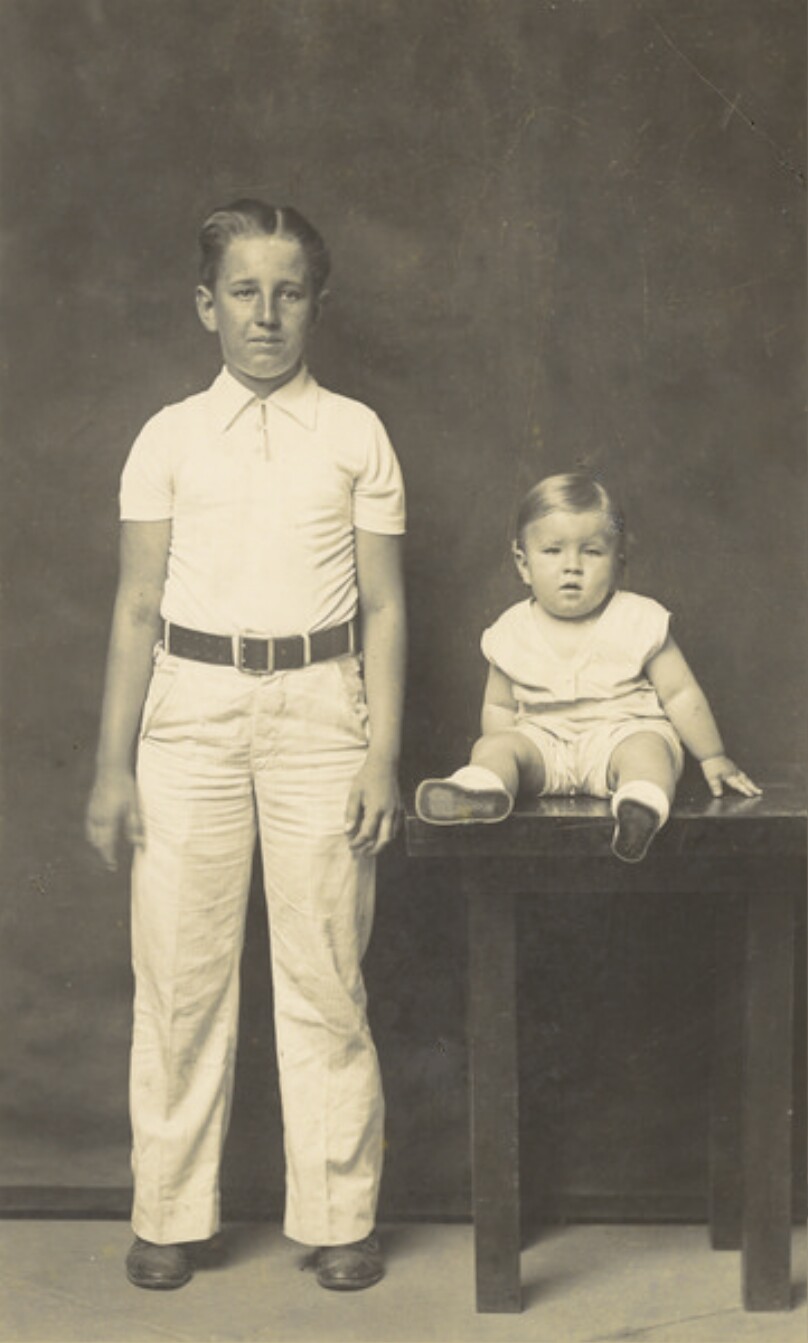 Untitled (older boy, standing, with toddler, seated on table)