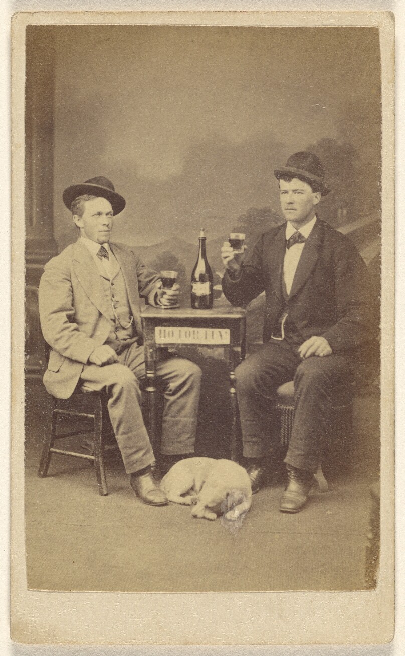 [Two men drinking at a table, a dog lying at their feet]
