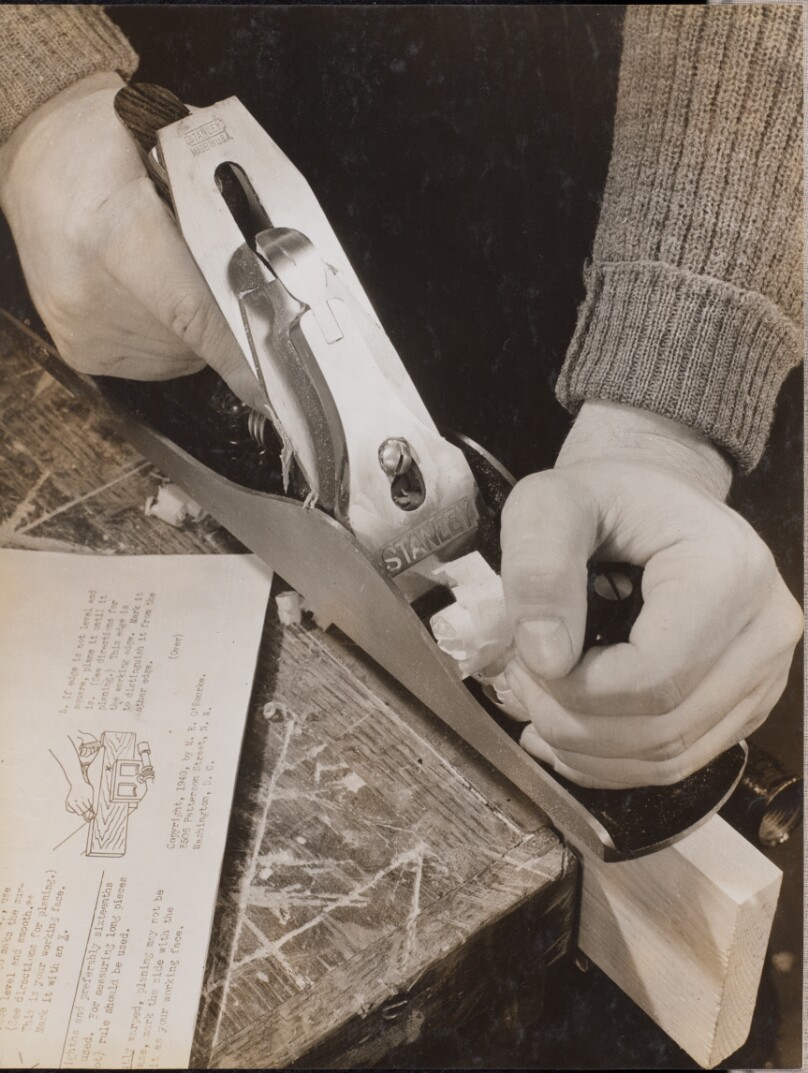 [Man uses a wood plane with an instruction booklet sitting to the left]