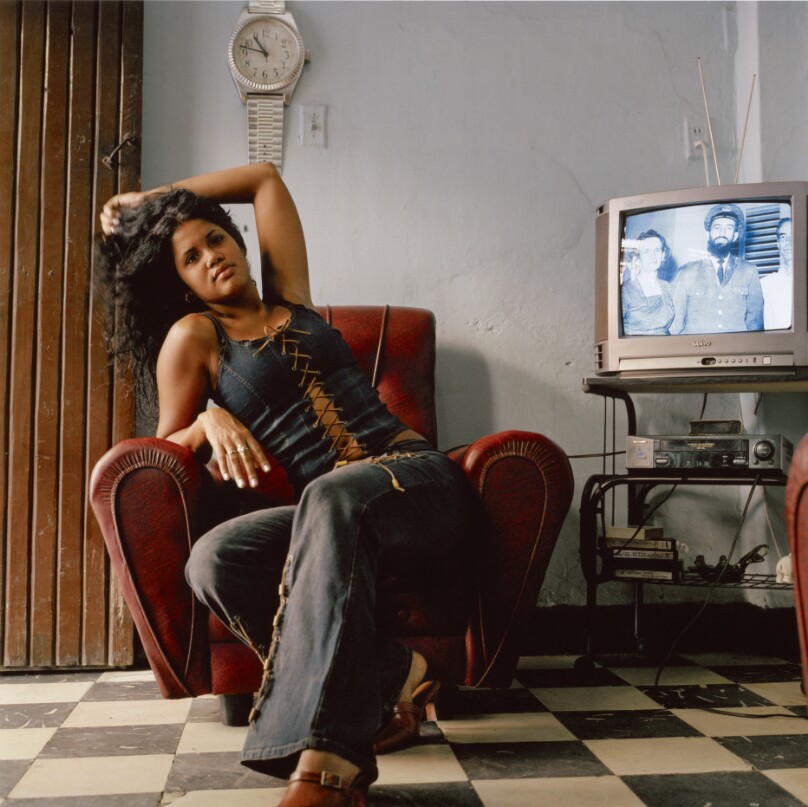 Woman Posing in Her Living Room, with Camilo Cienfuegos on the TV