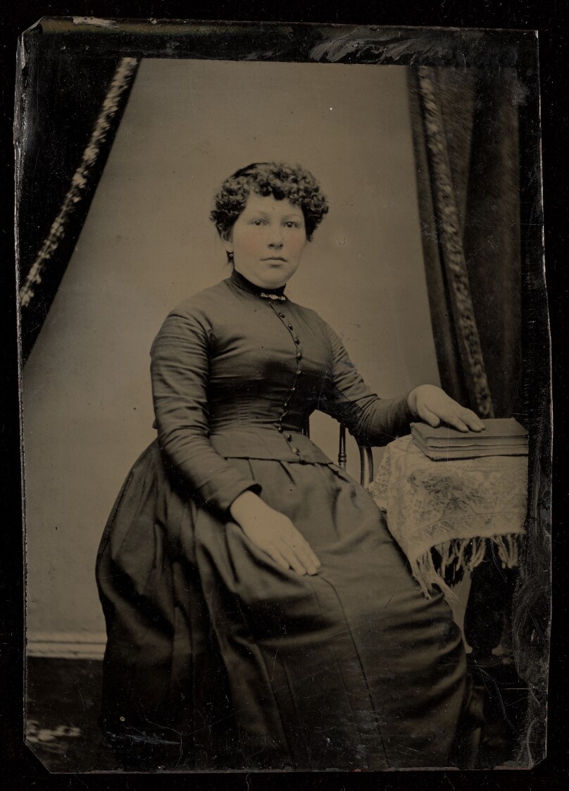 [Unidentified woman seated, hand on book on a small table]