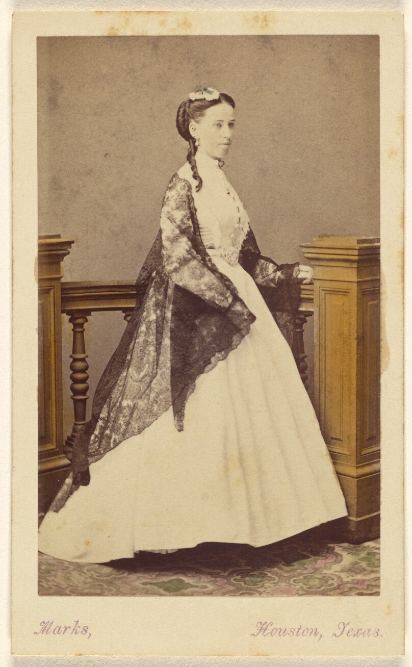 [Unidentified woman wearing a white dress and black shawl, standing]