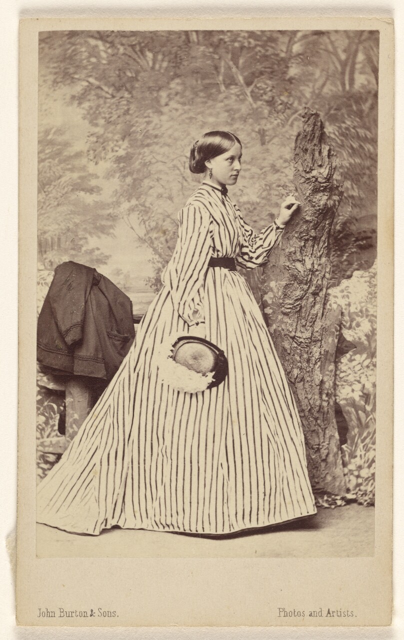 [Unidentified woman wearing a striped dress, holding a hat, standing]