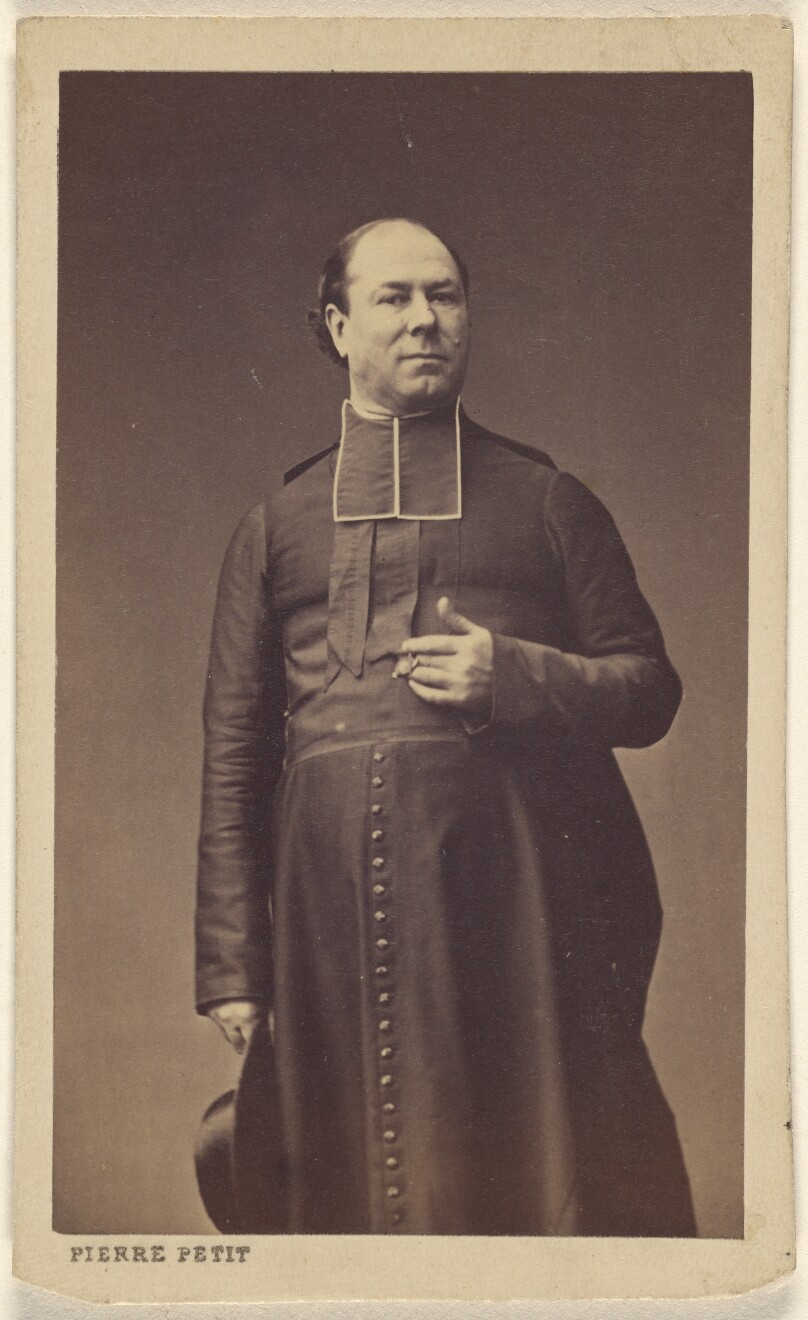 [Unidentified clergyman standing, holding a hat]