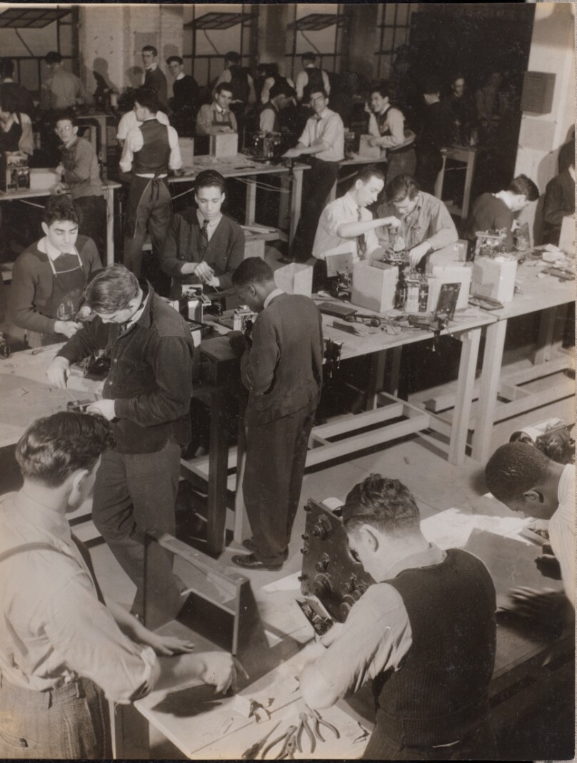 [Large group of young men work on machines]