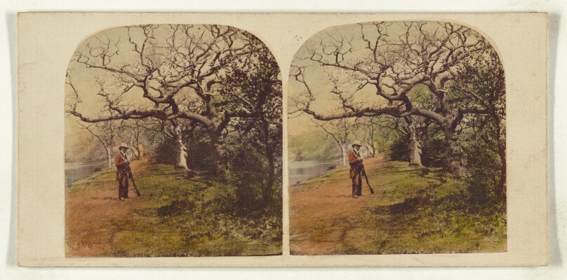 [Man in hunting outfit with hat standing, holding shotgun]