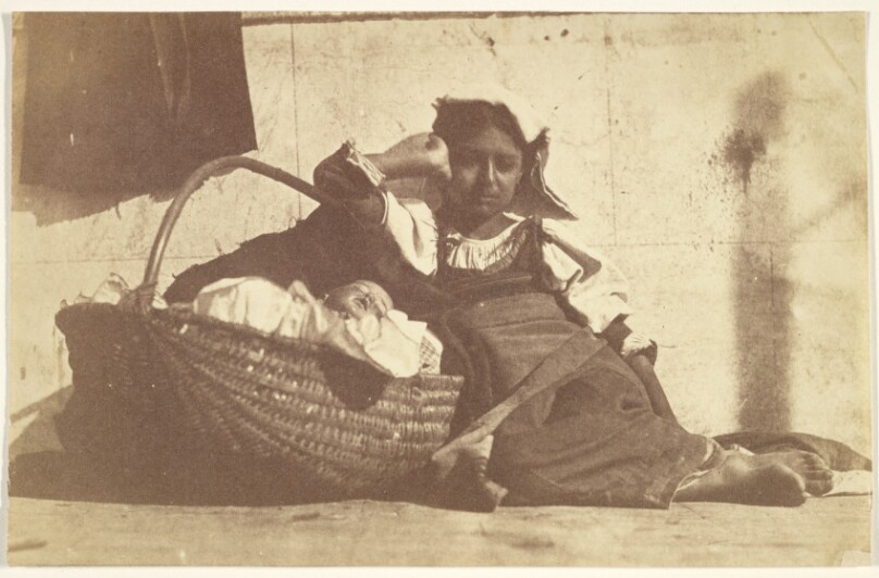[Barefoot girl leaning on basket with a doll]