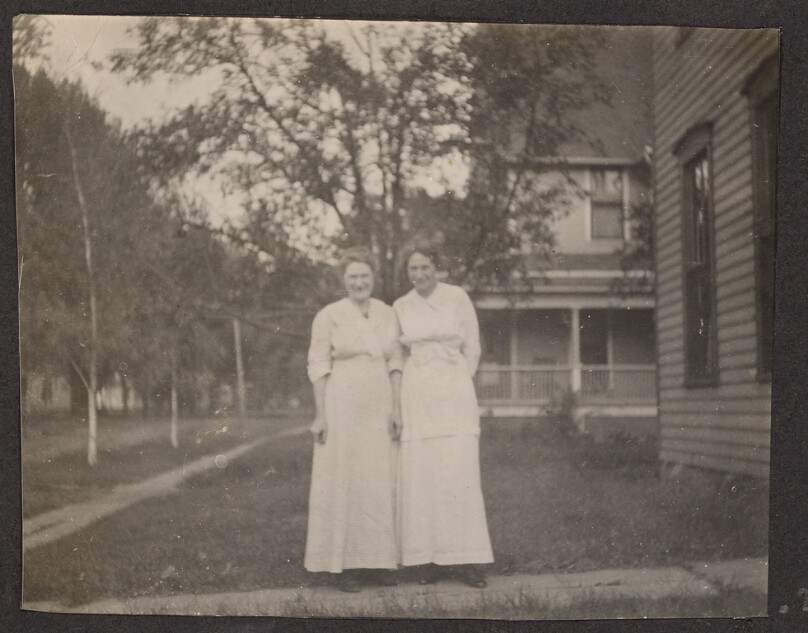 [Two women pose on a sidewalk]