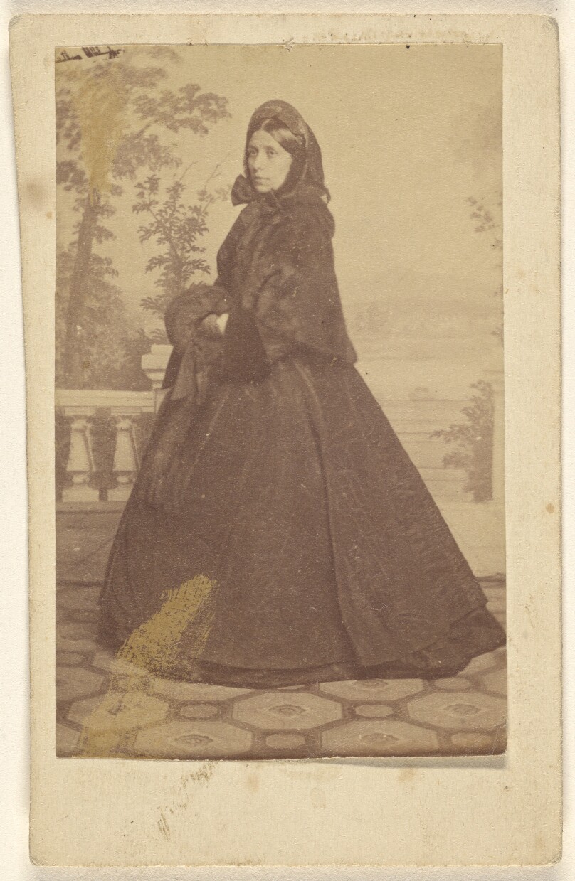 [Unidentified woman wearing a long dress with veil and muff, standing]