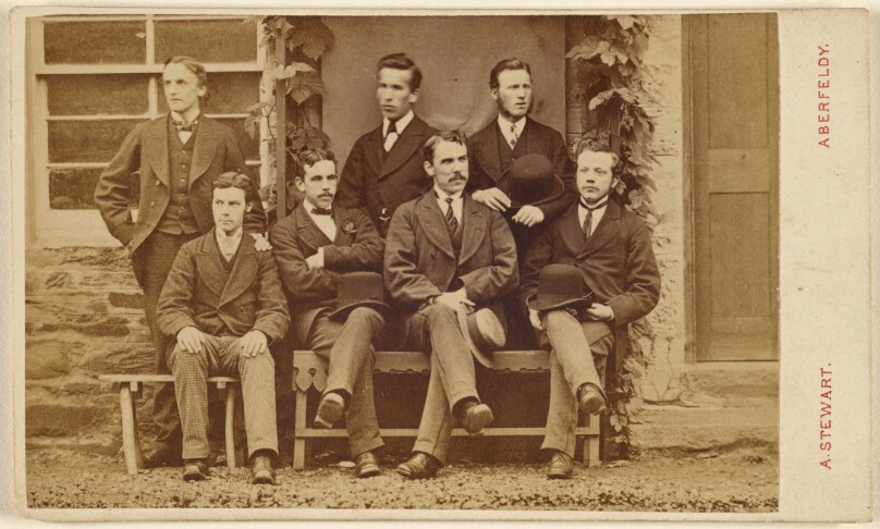 [Group of seven unidentified men: four seated, three standing, some holding hats]