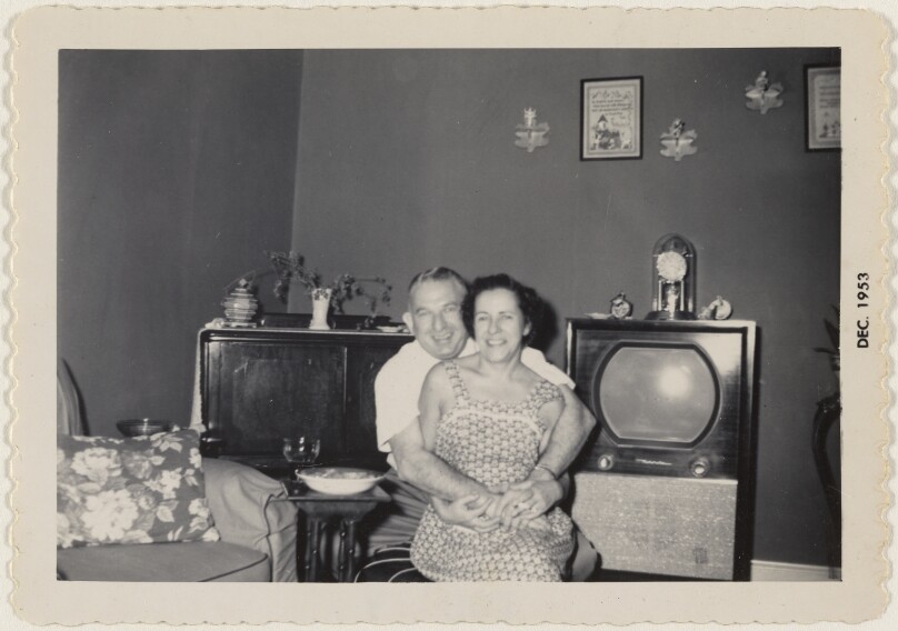 [Man and woman hugging in front of television set]