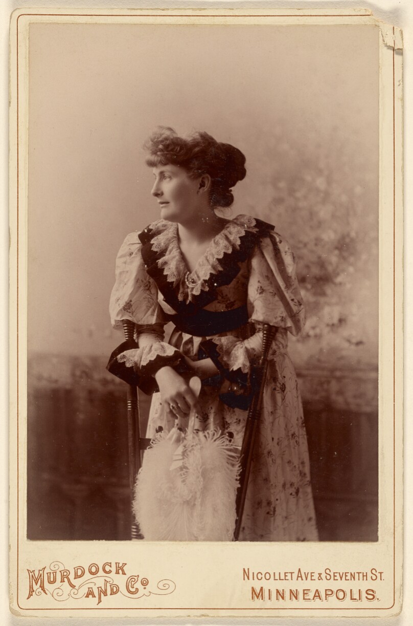 [Unidentified woman in profile, leaning on a chair, holding a feather fan]